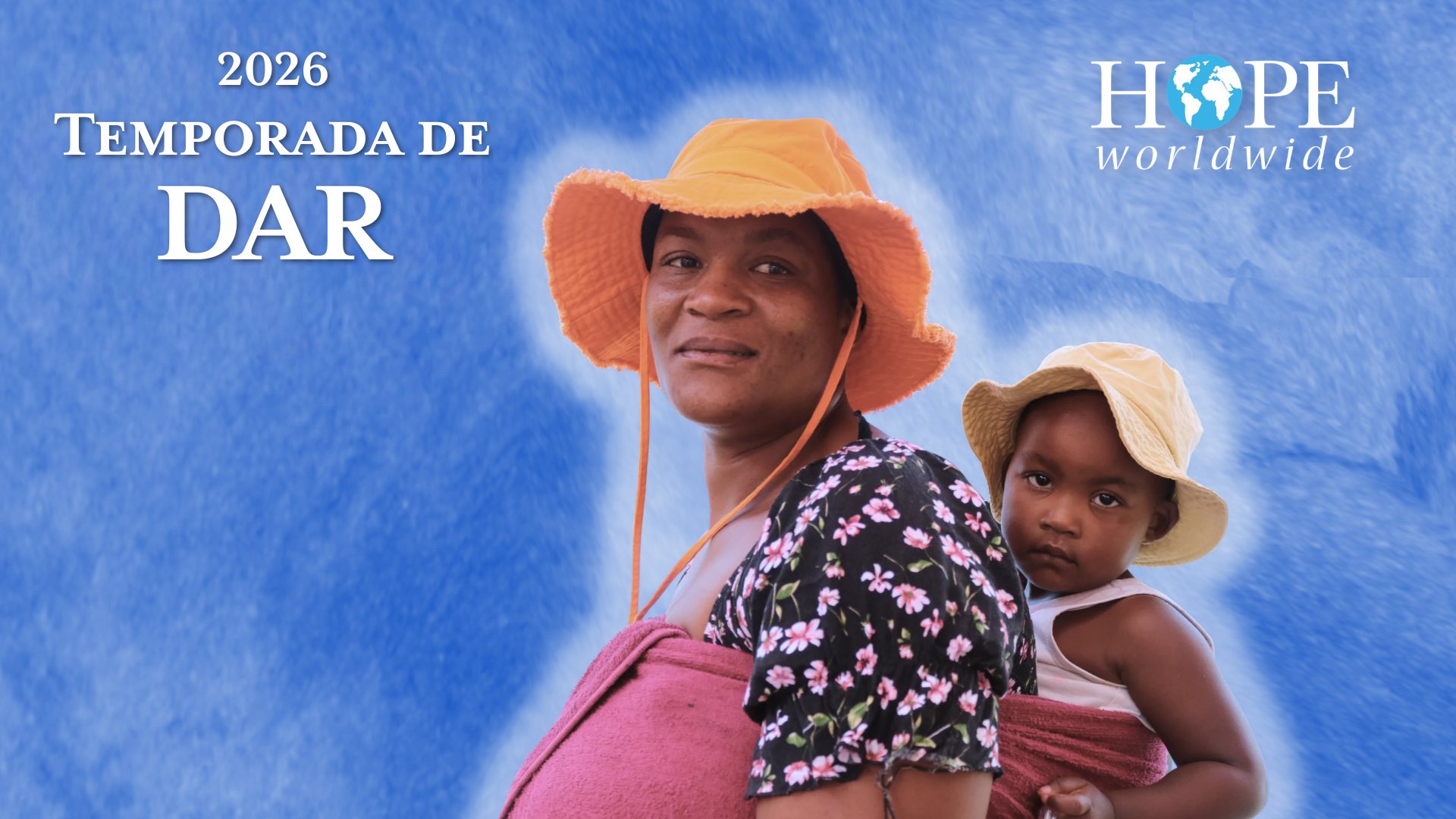 Temporada de Dar 2026, HOPE worldwide. Una madre con sombrero naranja mira por encima del hombro mientras carga a su hijo pequeño en la espalda.
