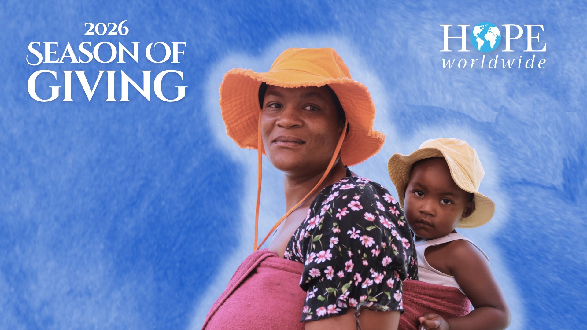 2026 Season of Giving, HOPE worldwide. A mother in an orange hat looks back over her shoulder, carrying her young child on her back.