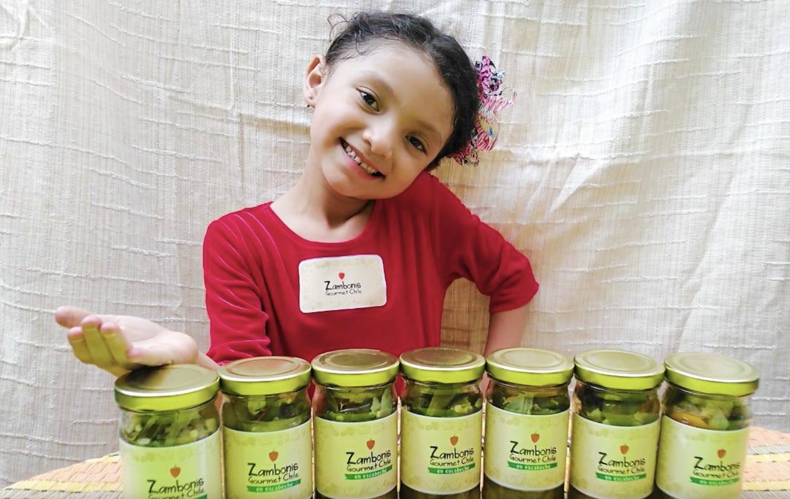 Valerie smiling behind a row of jars labeled Zambonis Gourmet Chile.
